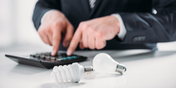Persona calculando el coste de la factura de luz por horas con una bombilla sobre la mesa